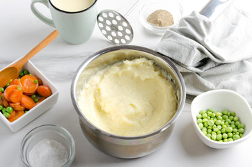 Delicious mashed potatoes in pot, bowls with different spices, vegetables and cup of milk.Tasty and healthy food