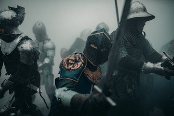 Squad of medieval knights of the Crusaders during the battle with swords in misty morning.