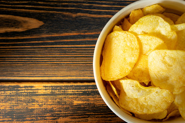 Golden potato chips on wooden background.