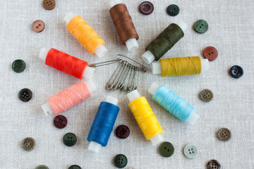 Fototapeta na wymiar sewing tools: colored sewing threads, safety pins, small colored buttons on a light gray background close-up, selective focus