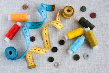Fototapeta na wymiar sewing tools: colored threads for sewing, centimeter ribbons, small colored buttons on a light gray background close-up, selective focus