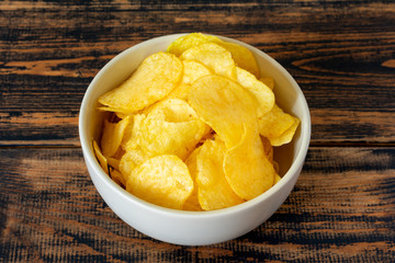 Golden potato chips on wooden background.