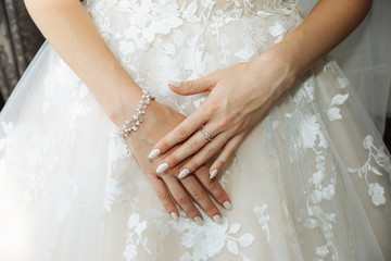 Beautiful bride's hands on the dress. Fingers with golden rings. Wedding morning.