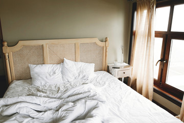 Bed with white sheets and vintage nightstand with decor at window  in hotel room or provence home bedroom. Space for text. Enjoying morning concept