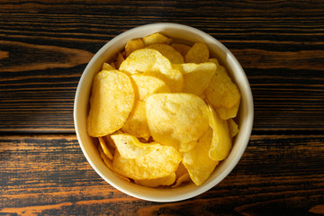 Golden potato chips on wooden background.