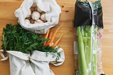 Ban plastic. Choose plastic free. Reusable eco friendly bag with fresh carrots,mushrooms,arugula and celery in cellophane plastic package on wooden table, flat lay. Zero waste grocery shopping