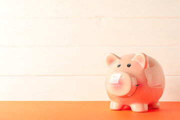 Happy piggy bank on color table against white wooden background, space for text. Finance, saving money