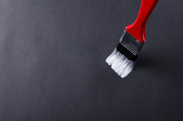Close up of red paint brush with black bristle and white paint on it.Black surface and empty space