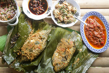 Traditional Indonesian cuisine. Grilled fish with spices served on the banana leaf with sauces and side dishes 