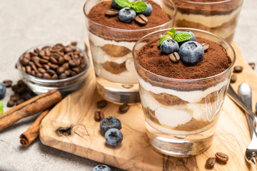 Classic tiramisu dessert in a glass with blueberries on concrete background