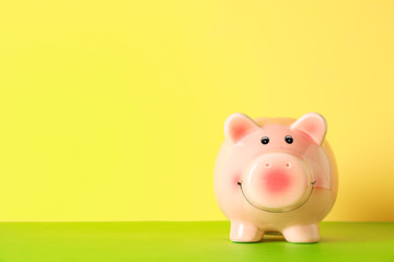 Happy piggy bank on color table against yellow background, space for text. Finance, saving money