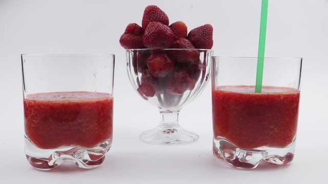 Drinking straw is dipped in a glass with freshly prepared strawberry juice on a white background