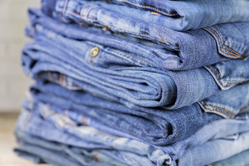 Stack of blue jeans on wooden shelf with copy space. Beauty and fashion clothing concept, selective focus