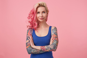 Portrait of positive cute lady with pink hair and tattooed hands, standing over pink background and...