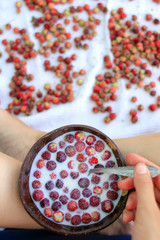 Wooden bowl with strawberries and milk in girl hand on light background, organic food and  healtly breakfast concept