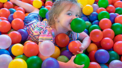 Fototapeta na wymiar A girl in the pool with many colored balls in the kids playing room