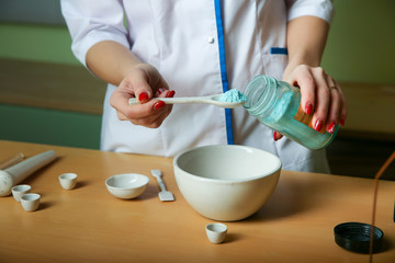 a lab technician conducts chemical experience. the hand of the chemist puts the powder into a bowl. a chemistry teacher is putting the matereal for experiments into a mortar