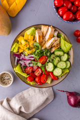 Grilled Chicken Mango Salad with cilantro, cucumbers, cherry tomatoes and red onion on gray background, top view