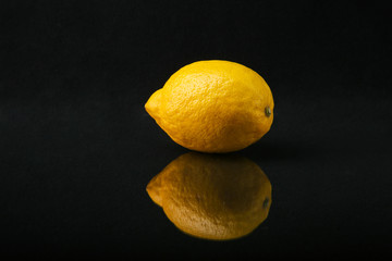 a whole lemon on a black background with reflection close up.