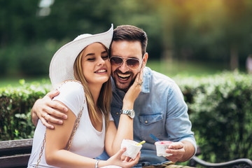 Couple joking and having fun while eating an ice cream in the park.