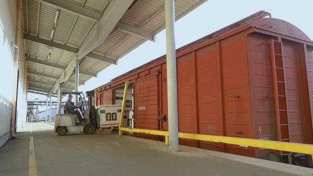 A large warehouse, forklift loads boxes in the freight train. Rail transportation