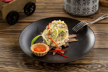 Traditional Russian salad Olivier with red caviar on brown plate on wooden table
