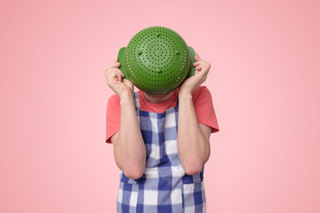 Man in apron holding colander near face hiding.