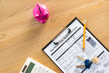 top view of clipboard with new house loan application form lettering on document near keys, pencil ,pink piggy bank and calculator
