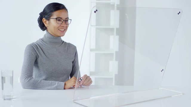 Lockdown of female Asian businesswoman sitting in office at invisible AR screen and having video conversation