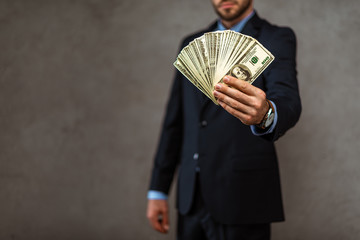 selective focus of businessman holding dollar banknotes on grey