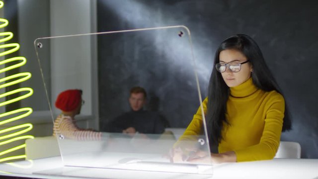 Lockdown of young Middle Eastern woman in casual wear sitting at caf&eacute; table at invisible multi-touch monitor of futuristic PC and typing on wireless keyboard. Video suitable for adding AR graphics