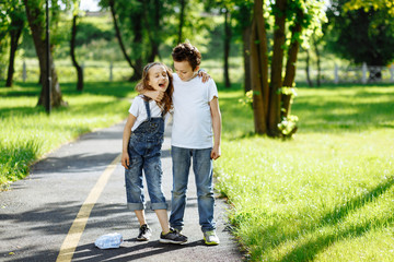 Obraz premium Picture of brother and sister having fun in the summer park on sunset. Cheerful children hugs and laughing. Little girl and boy playing outdoors, best friends, happy family, love and happiness concept