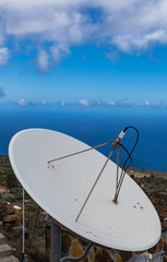 White aged satellite dish,with ocean and blue sky with white clouds horizon
