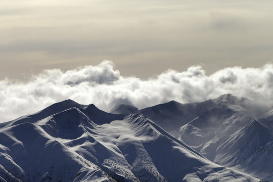 Snowy sunlit mountains in haze and cloudy sky at winter evening