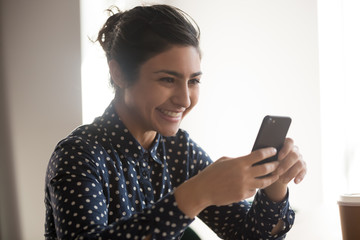 Close up of smiling indian woman typing message on smartphone