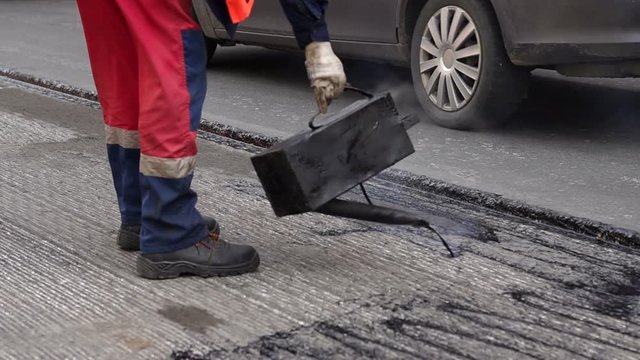 Road repair. Work details, workers pour resin road surface to cover the asphalt. Men in specialized clothing repair asphalt in the city. Preparation of asphalt pavement for laying new asphalt.