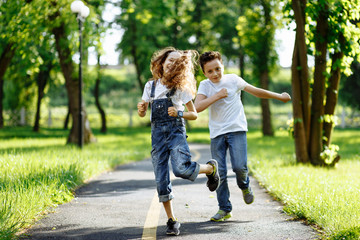Brother and sister running in the summer park on sunset. Cheerful children. Little girl and boy are doing sports outdoors, best friends. Childhood concept