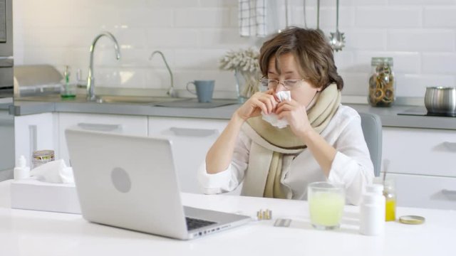 Lockdown of sick Caucasian woman sitting at laptop with napkin in her hands