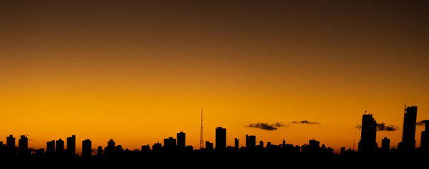 Naklejka premium Zachód słońca w mieście, kiedy pomarańczowe niebo kontrastuje z budynkami prostymi liniami.