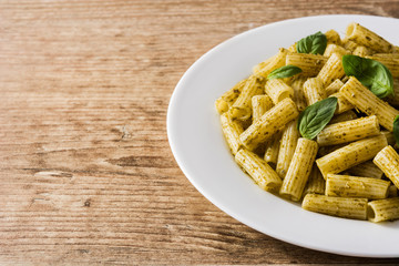 Penne pasta with pesto sauce and basil on wooden table