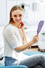 Lady checking teeth in mirror. Young female at dentist office.