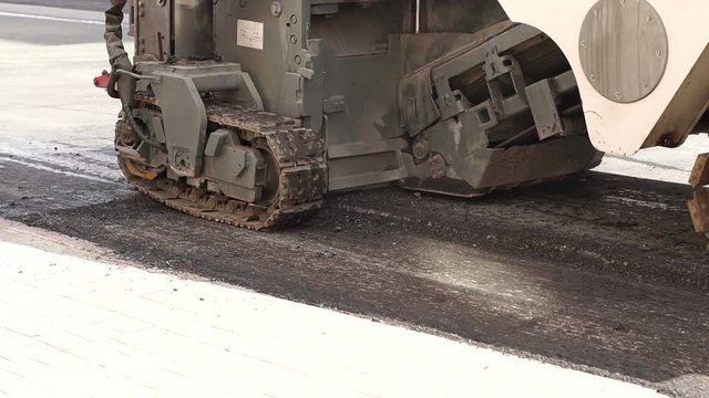 Road works. Dismantling of asphalt pavement. A fragment of a trimming unit-track. A large industrial tractor cuts off the old asphalt. Slow motion.
