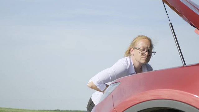 woman opens hood of car, expresses bewilderment and closes hood.