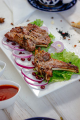 Barbecue ribs on white plate, meat dish served with onion and herbs.