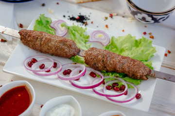 Meat kebabs on skewer over the white plate.