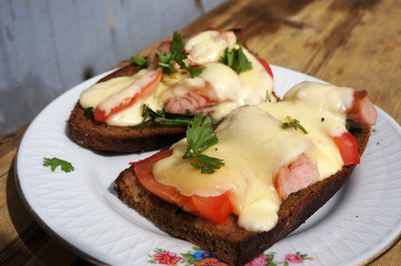 Hot cheese, tomatoes and sausages sandwiches on rye bread.