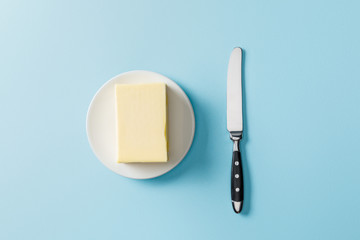 top view of butter on white plate and knife on blue background