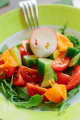 Salad with cherry potatoes, cucumber, raddish and lettuce in a green plate.