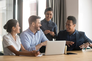 Smiling diverse employees talk brainstorming in office using laptop