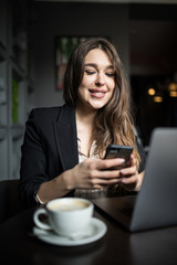 Charming woman with beautiful smile reading good news on mobile phone during rest in coffee shop. Caucasian female watching her photos on cell telephone while relaxing in cafe during free time
